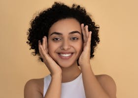 pexels-photo-6706841-6706841-1 Portrait of a smiling woman with curly hair, highlighting her fresh skin and happiness against a beige backdrop.